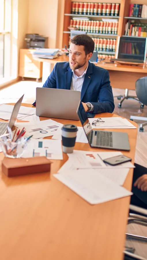Business professionals discussing work over laptops and documents in a bright office meeting room.