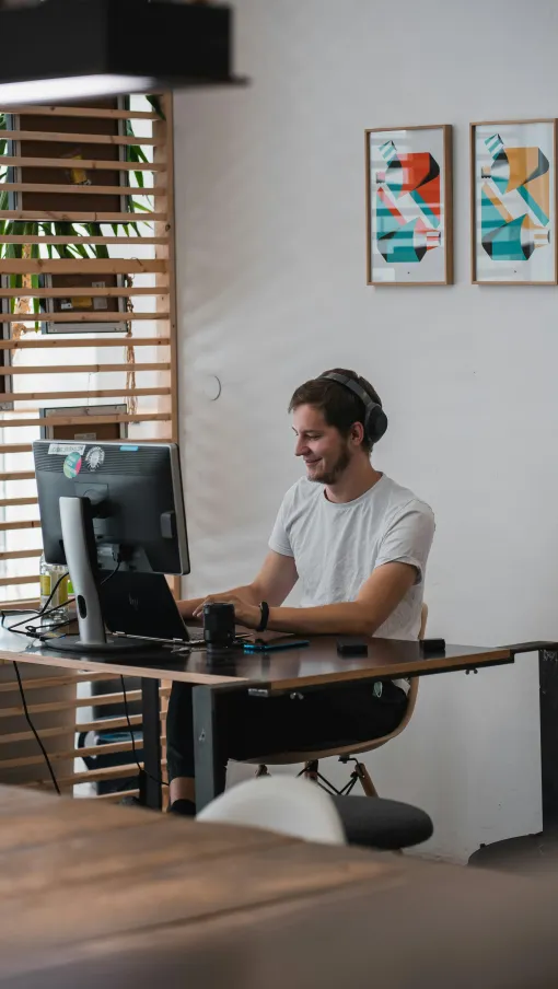 Man wearing headphones working on computer at modern desk in bright, minimalist office with abstract art.