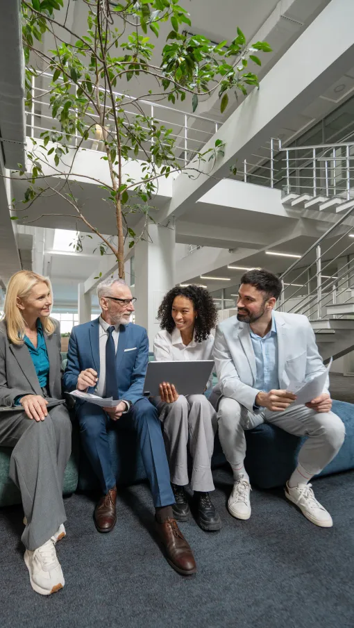 Diverse business team sitting in modern office lounge discussing work with a laptop and documents
