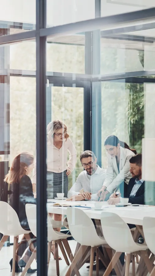 Business team collaborating and discussing documents in a modern glass office meeting room.