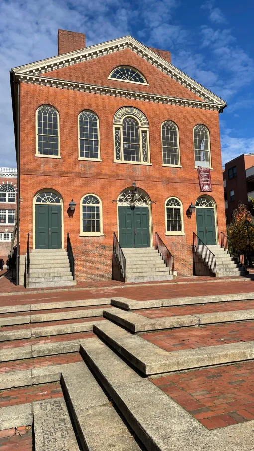 Historic red brick town hall with green doors and arched windows under a blue sky with stairs in front.
