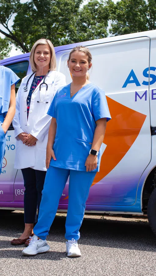 Five medical professionals in scrubs and lab coats stand in front of an Ascend Medical branded van outdoors.