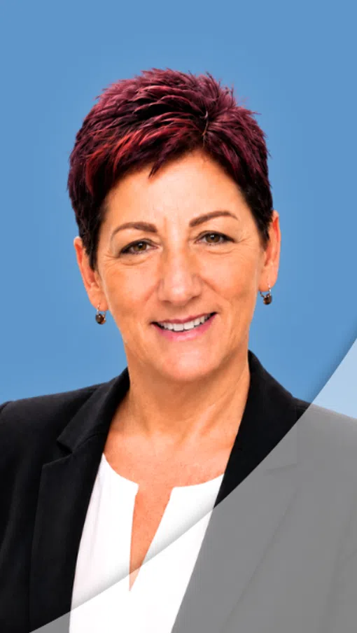 Professional woman with short red hair smiling, wearing black blazer and white top against blue background.
