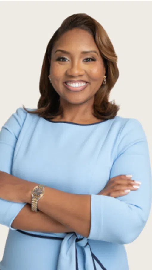 Confident woman in light blue dress smiling with arms crossed against light background