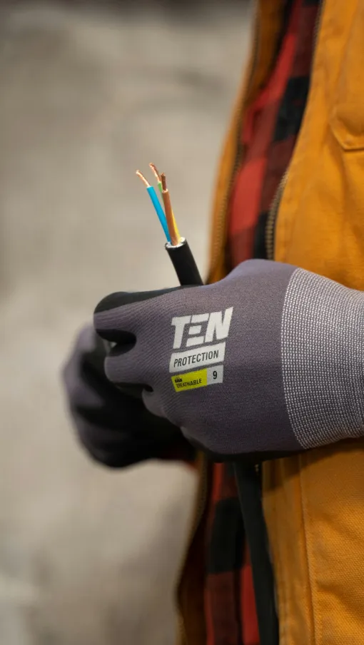 Electrician hand in protective glove holding stripped electrical wire indoors, wearing orange vest and plaid shirt Ball Ground