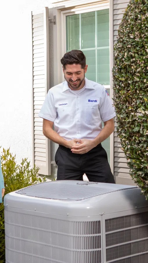 A Bardi installation technician explains an outdoor HVAC unit to a homeowner outside a house.