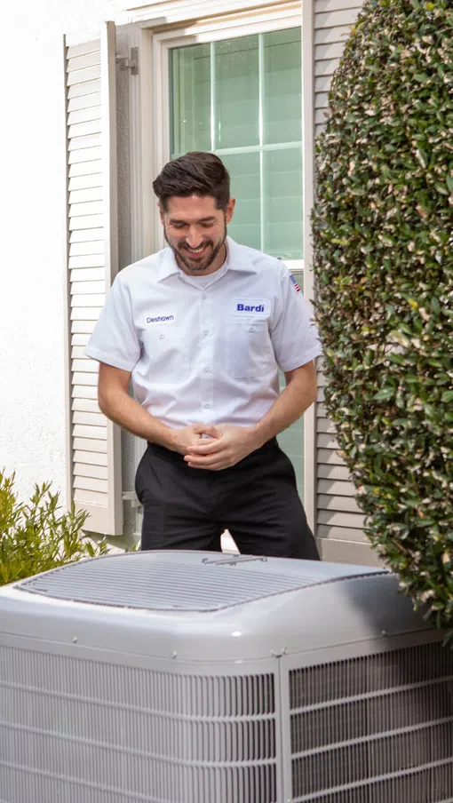 A technician explains an air conditioning unit to a homeowner outside a house.