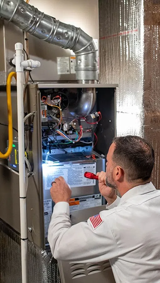 Technician inspecting a residential heating system in a well-lit utility room.