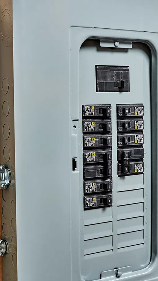 Open electrical panel box with circuit breakers and yellow electrical wires on wooden wall background.