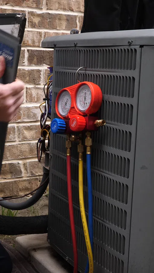 HVAC technician inspecting outdoor heat pump unit with pressure gauges attached to system.