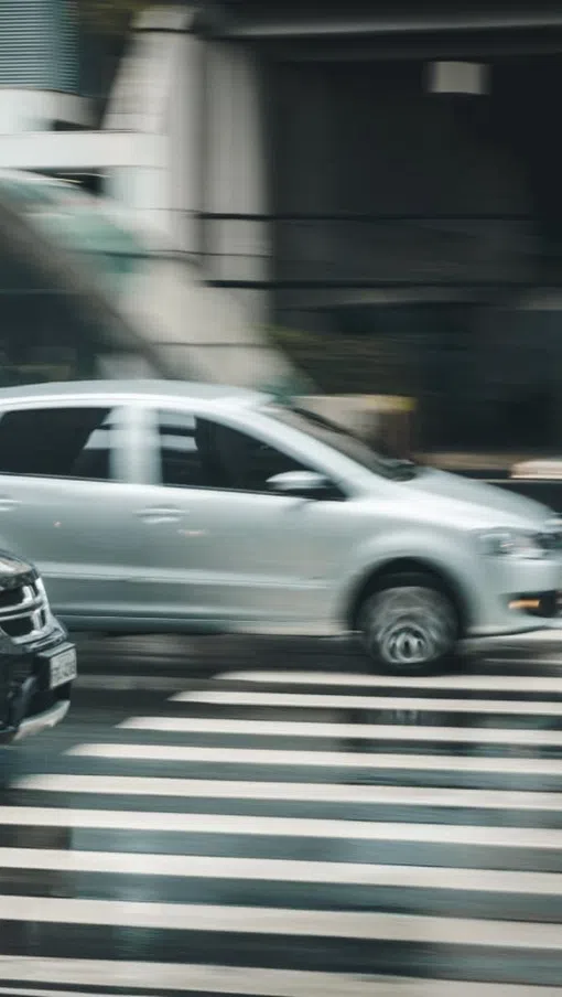 Blurred motion of silver and black cars driving over a striped pedestrian crosswalk in an urban setting.