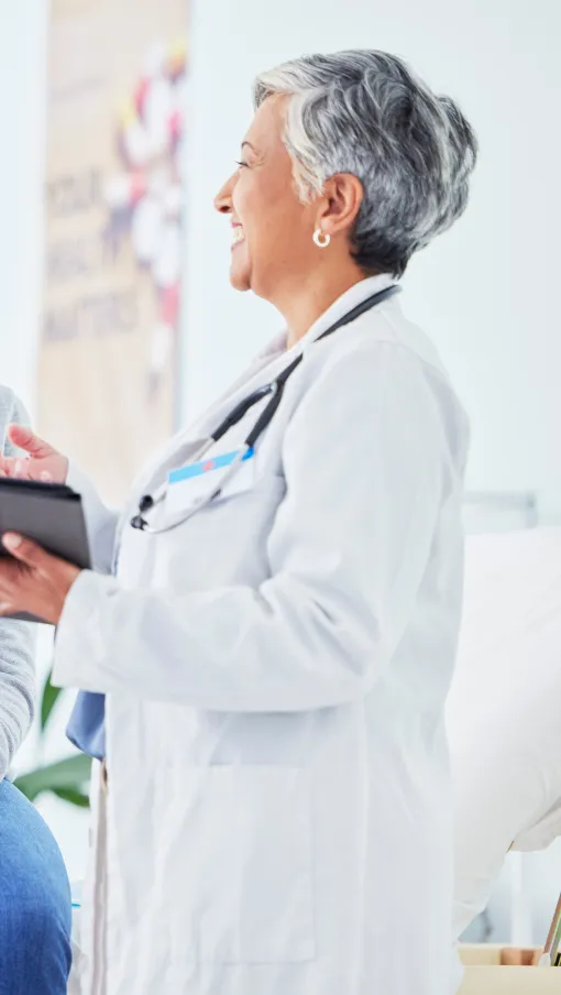 Doctor with tablet consulting smiling patient in medical office during a health checkup
