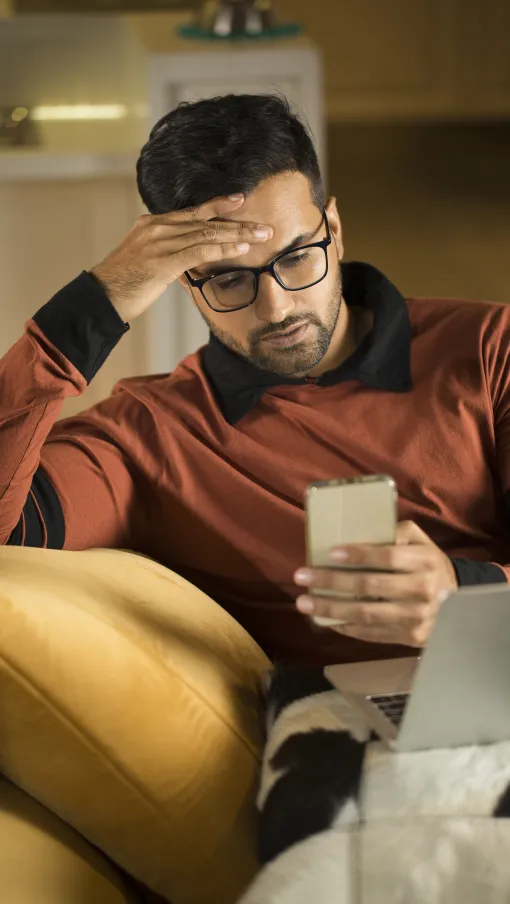 a man holding a phone and looking at a laptop