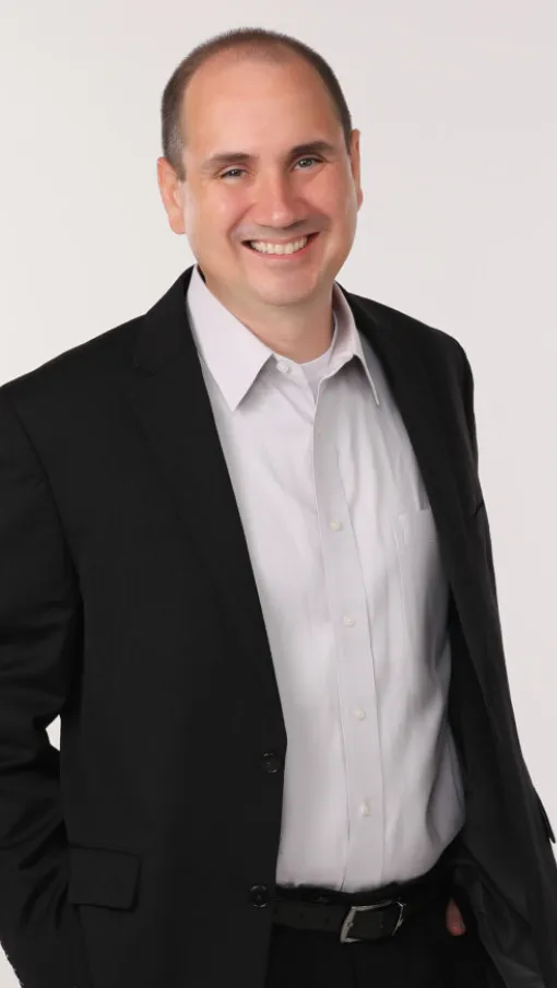 Smiling man in black suit and white shirt posing against a plain white background
