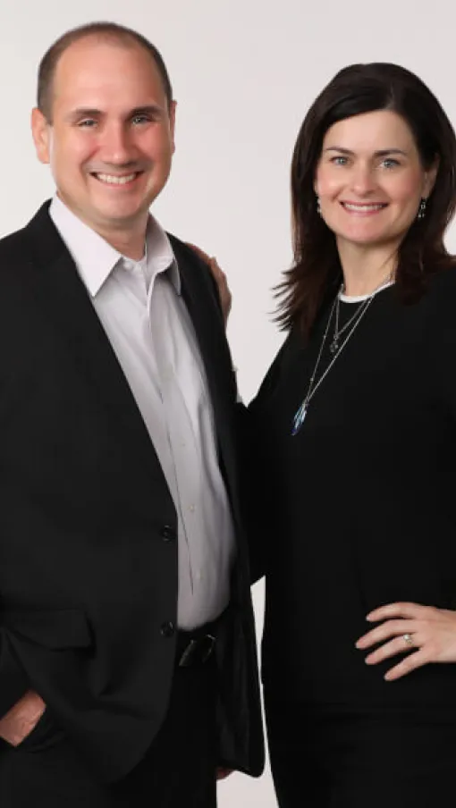 Smiling man and woman in formal black and white attire posing together against white background