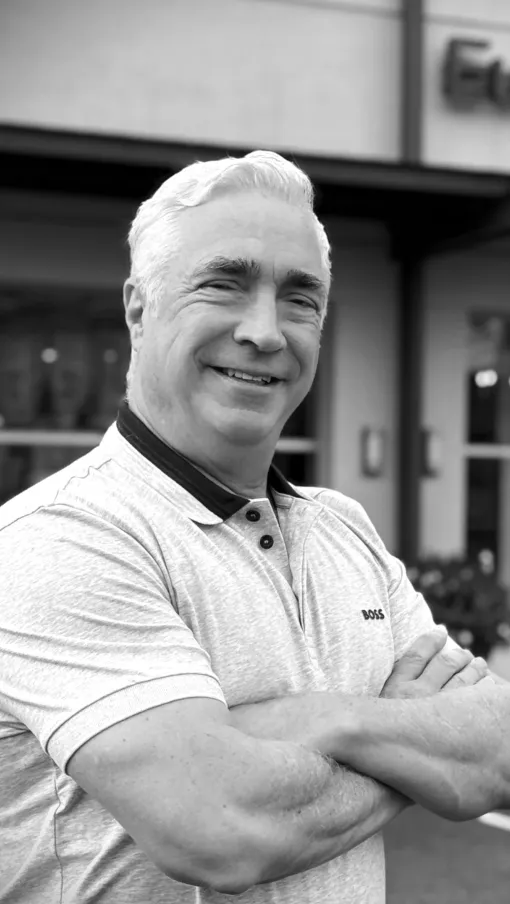 Smiling middle-aged man with crossed arms standing outside a store named European in black and white