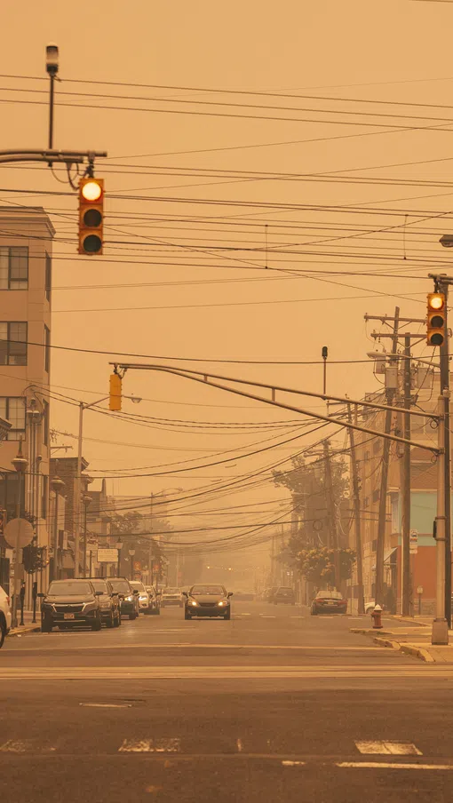 Urban street with traffic lights glowing orange and hazy atmosphere caused by smoke or fog covering buildings and vehicles.