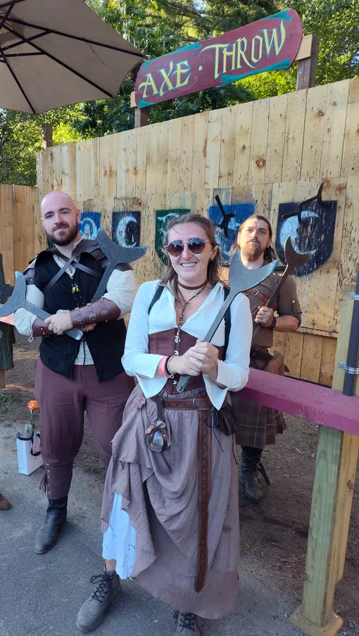 Four people in medieval costumes holding axes at an outdoor axe throwing venue with wooden target boards.