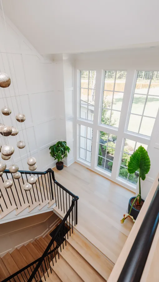 Bright staircase with black railing, large windows, hanging globe lights, and indoor potted plants in modern home