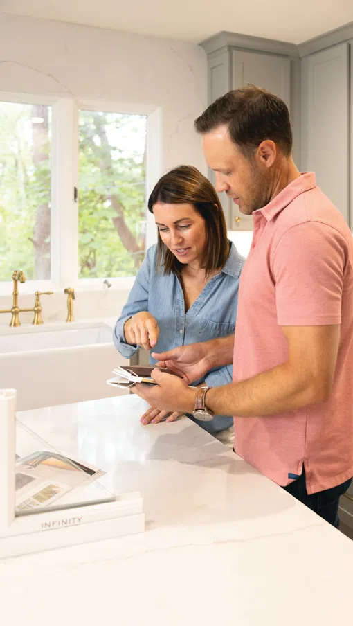 Couple choosing color samples for kitchen remodel in bright modern kitchen with gray cabinets and marble countertops