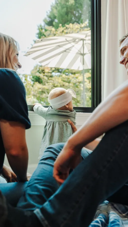 Parents watch their baby standing by the fiberglass window looking outside