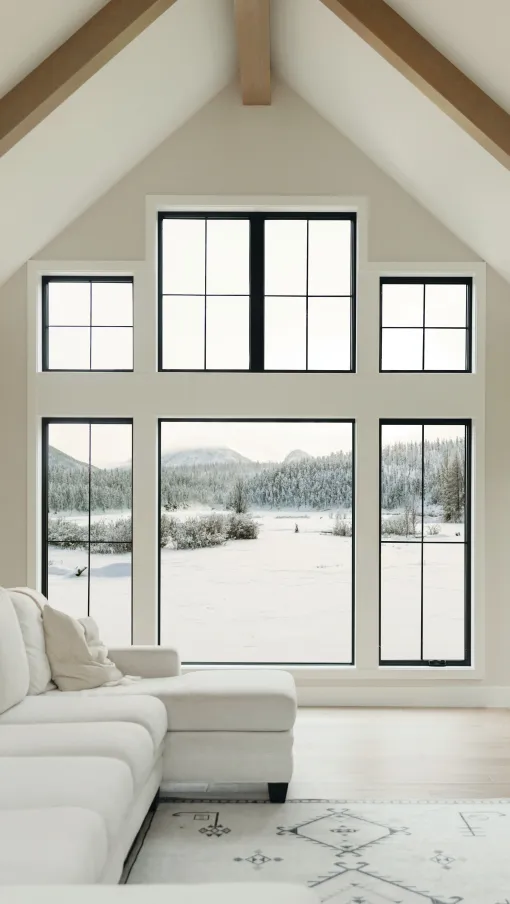 Bright modern living room with large black-framed windows showcasing a snowy mountain landscape outside.