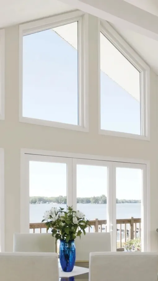 Spacious sunlit dining area with large windows overlooking a serene lake and wooden deck outside.