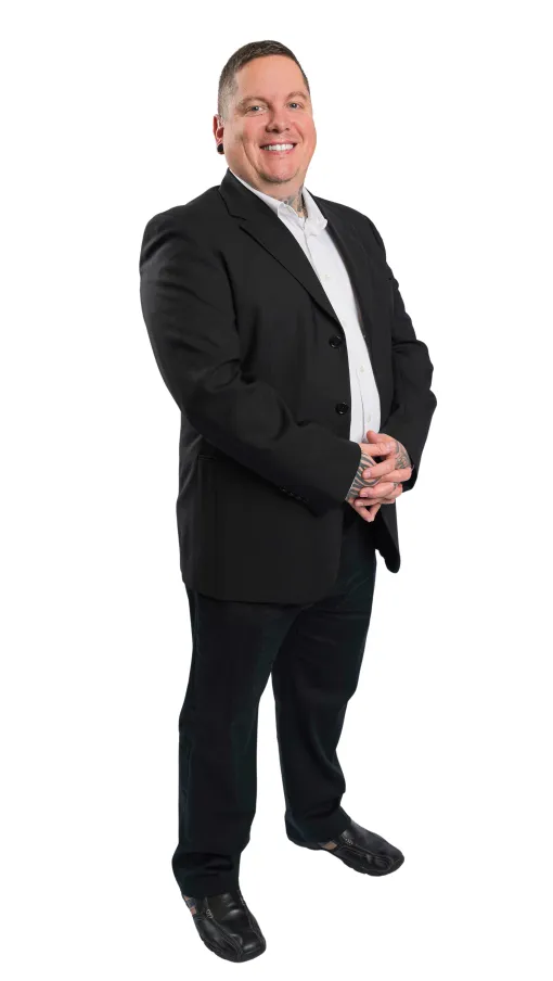 Smiling man in black suit and white shirt standing with hands clasped against white background