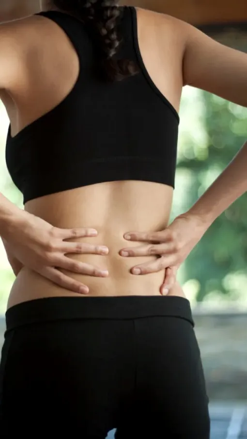 Woman in black sportswear holding lower back in pain, possibly due to injury or muscle strain.