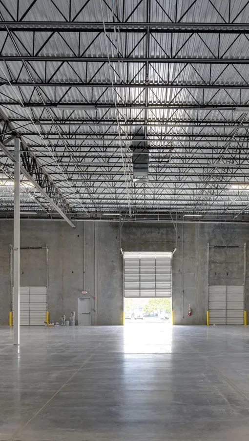 Empty industrial warehouse interior with concrete floors, high ceilings, and multiple loading dock doors.