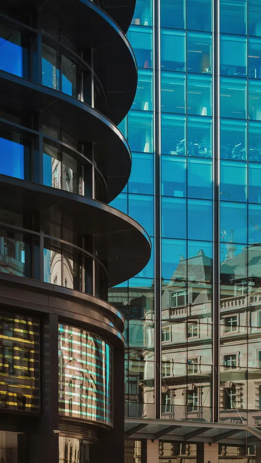 Modern curved glass building reflecting classic architectural details of nearby structures under clear sky.
