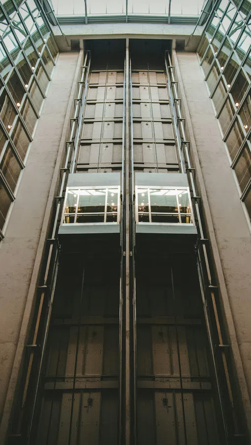 Two glass elevators inside a modern building with reflective windows and metal framework.