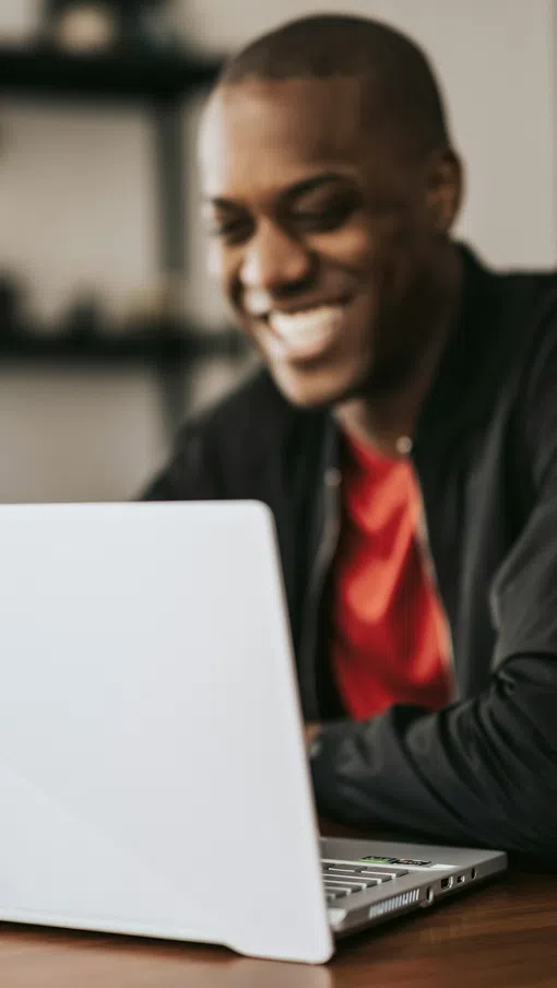 Two young adults smiling and looking at a laptop screen together in a bright room near a table.