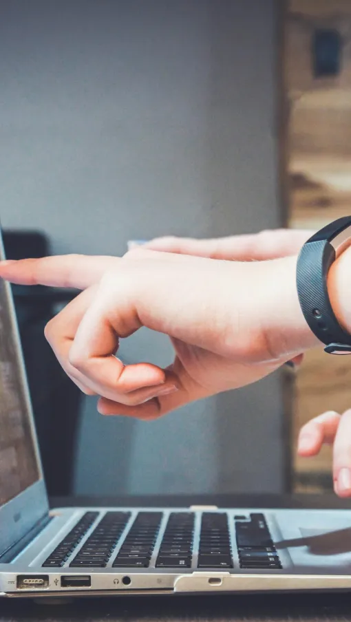 Two people collaborate using a laptop, one pointing at the screen while the other types on the keyboard indoors.