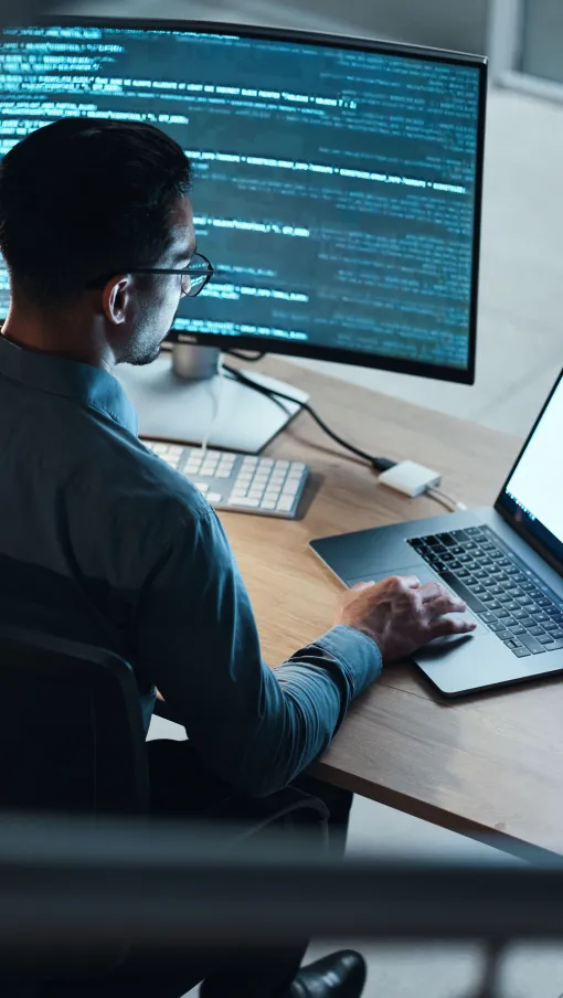 a person sitting at a desk with a laptop and a computer
