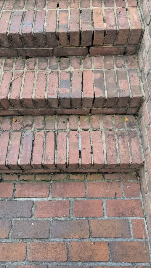 Close-up of weathered brick steps showing cracks and aged mortar with surrounding brick wall corner.