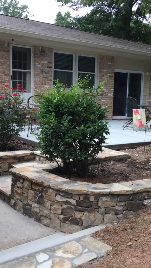 Beautiful backyard patio with stone walls, plants, and a seating area surrounded by greenery.