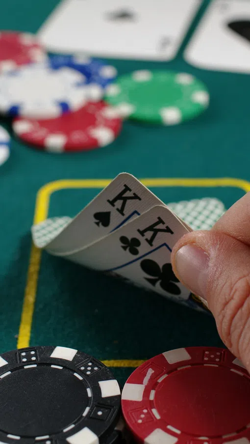 Hand holding two king playing cards on a poker table with chips and cards in the background.