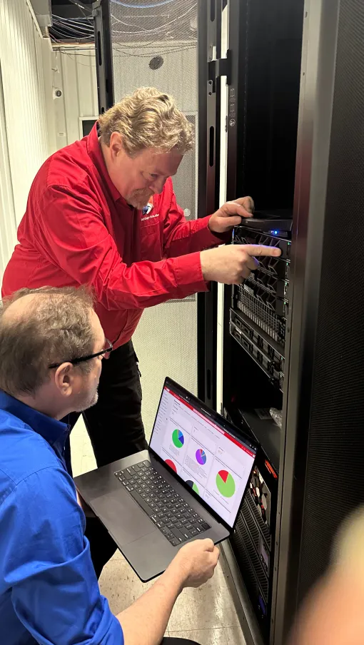 IT professionals troubleshoot server equipment while analyzing data charts on a laptop in a data center.