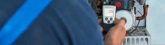 Technician using digital multimeter to test and measure electrical components on heating system equipment.