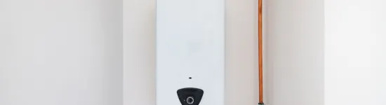 White tankless water heater mounted on wall with copper pipes and exhaust vent pipe.