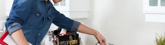 Plumber inspecting kitchen sink faucet with toolbox and wrench on countertop in modern white kitchen