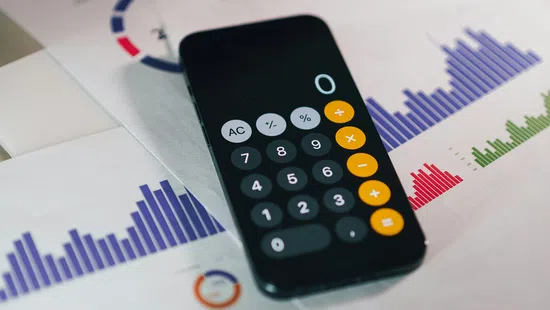 Smartphone calculator app on printed financial charts with colorful graphs and data visualizations.