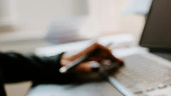 Close-up of hands using a wireless mouse and typing on a laptop keyboard in a bright office.