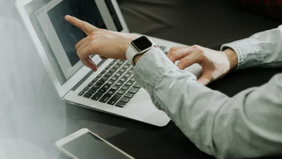 Two people collaborating over laptops and smartphone, one pointing at a laptop screen during discussion.