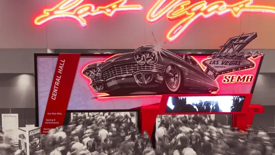 Neon-lit Las Vegas sign with classic car illustration and crowded convention hall at SEMA event.
