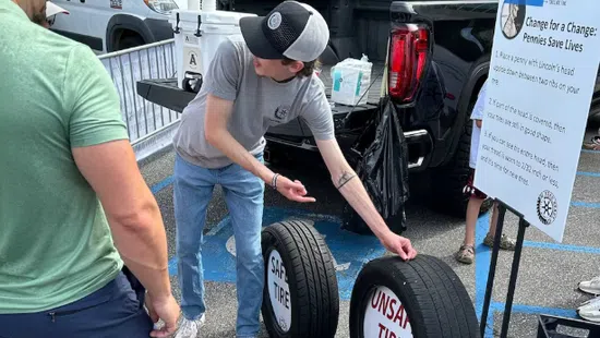Man explaining safe and unsafe tire comparison using real tires at outdoor event in parking lot.