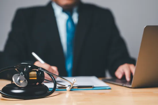 Doctor in suit writing notes with stethoscope and laptop on wooden desk in medical office