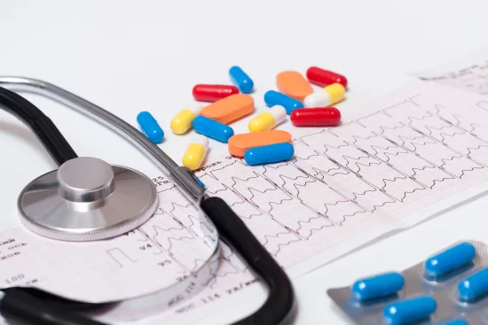 Stethoscope, assorted pills, and ECG heart rate chart on white background representing healthcare and cardiology.