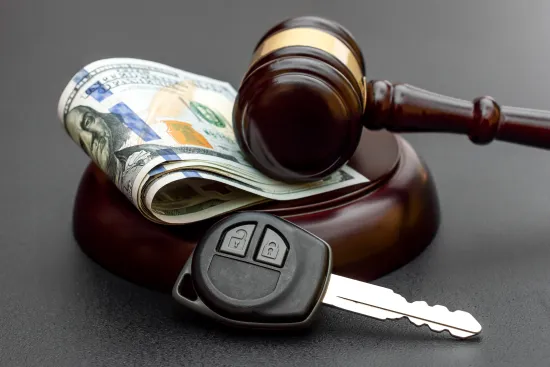 Judge gavel with rolled US dollar bills and a car key on a black surface representing legal and financial matters.